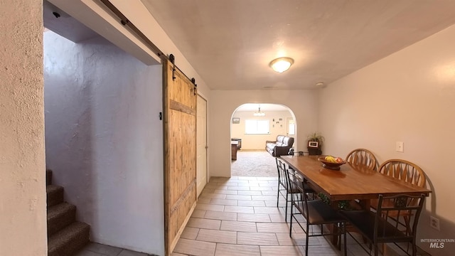 dining room featuring arched walkways, a barn door, and stairs