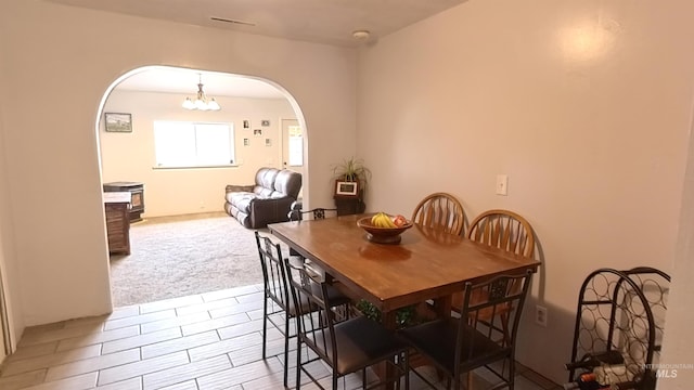 carpeted dining area featuring a chandelier and arched walkways