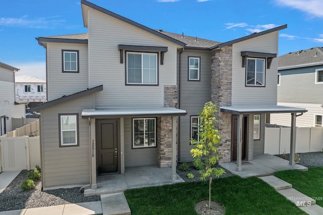 view of front of house with stone siding, a patio area, fence, and a front yard