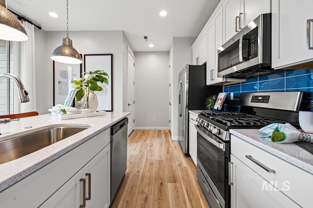 kitchen featuring decorative light fixtures, appliances with stainless steel finishes, white cabinets, a sink, and light stone countertops