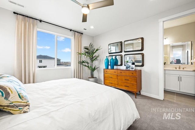 bedroom featuring baseboards, visible vents, light colored carpet, ensuite bathroom, and a sink