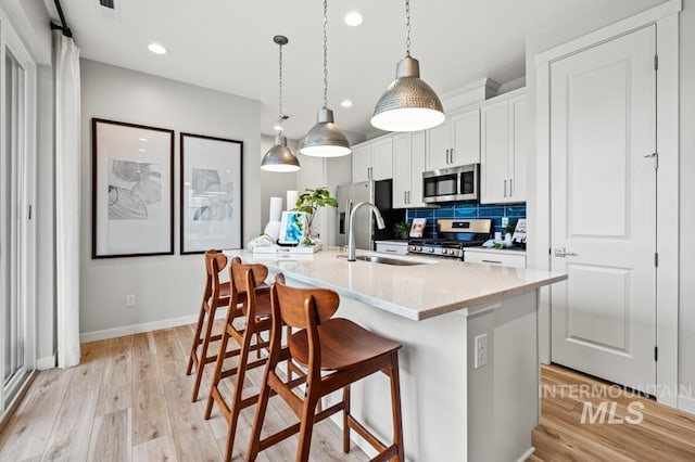 kitchen featuring stainless steel appliances, a sink, white cabinetry, an island with sink, and decorative light fixtures