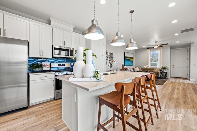 kitchen with stainless steel appliances, white cabinets, a kitchen island with sink, and hanging light fixtures