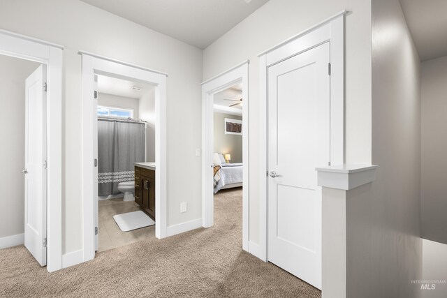 hallway featuring light colored carpet and baseboards