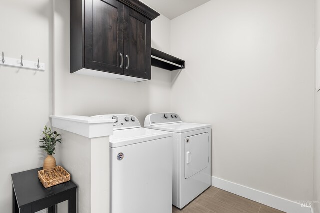 washroom featuring separate washer and dryer, light wood-style flooring, cabinet space, and baseboards