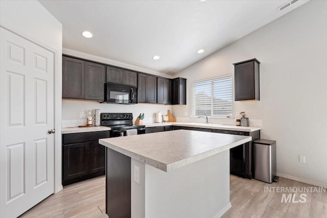 kitchen featuring a sink, light wood-style floors, light countertops, lofted ceiling, and black appliances
