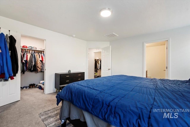 carpeted bedroom with visible vents and a walk in closet