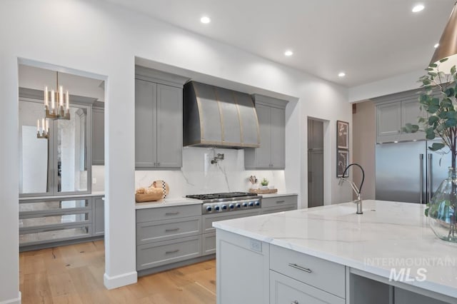 kitchen featuring stainless steel appliances, a sink, wall chimney range hood, gray cabinets, and light stone countertops