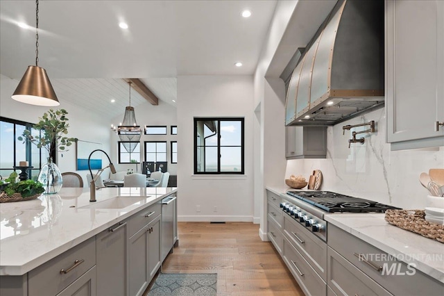 kitchen with stainless steel appliances, wall chimney range hood, a sink, and gray cabinetry