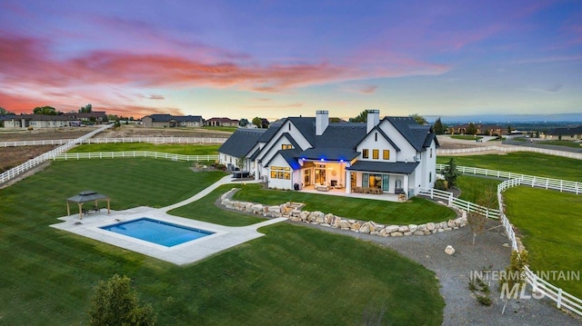 back of house at dusk featuring a rural view, a fenced backyard, a jacuzzi, a yard, and a patio area