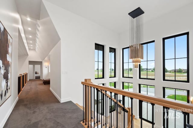 hall featuring baseboards, a high ceiling, an upstairs landing, and an inviting chandelier