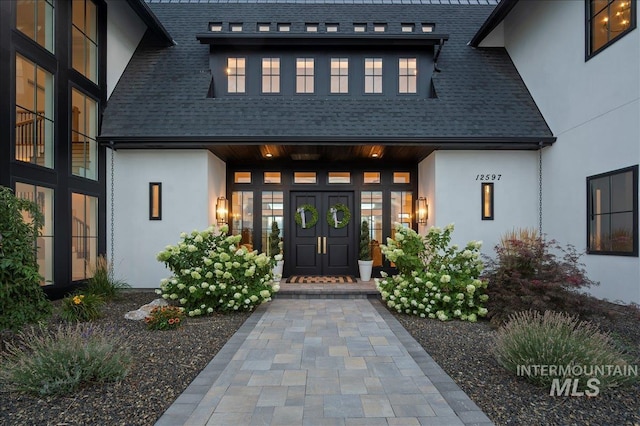 doorway to property featuring roof with shingles and stucco siding