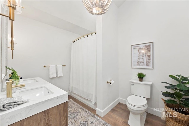 bathroom with toilet, wood finished floors, a sink, baseboards, and an inviting chandelier