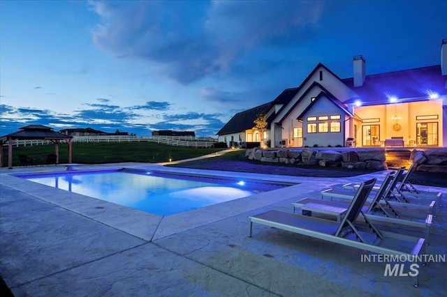 pool at dusk featuring a gazebo, fence, an outdoor pool, and a patio