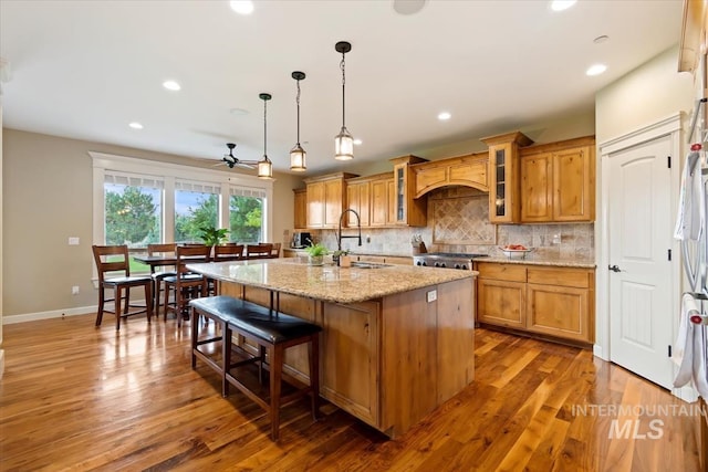 kitchen with pendant lighting, sink, backsplash, light stone countertops, and a center island with sink