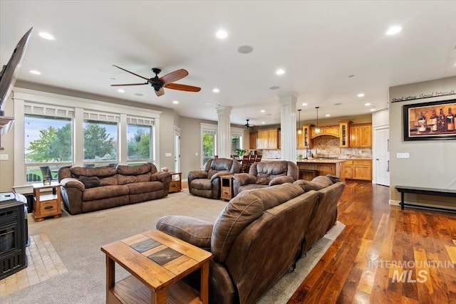 living room with dark wood-type flooring, ceiling fan, a wood stove, and ornate columns