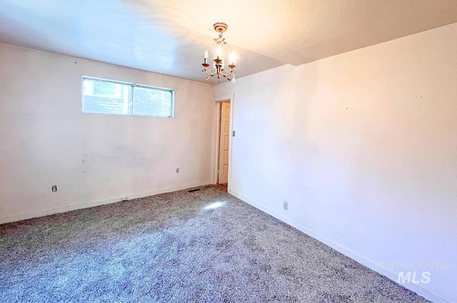 empty room featuring a chandelier, carpet, and baseboards