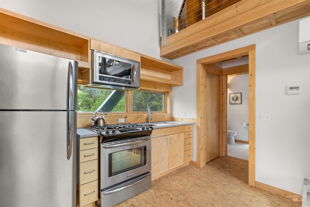 kitchen with appliances with stainless steel finishes, a sink, open shelves, light brown cabinetry, and light stone countertops