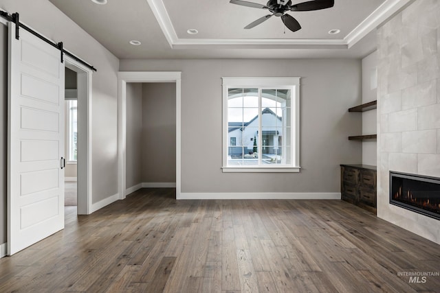 unfurnished living room featuring ceiling fan, a barn door, a fireplace, a raised ceiling, and dark hardwood / wood-style flooring