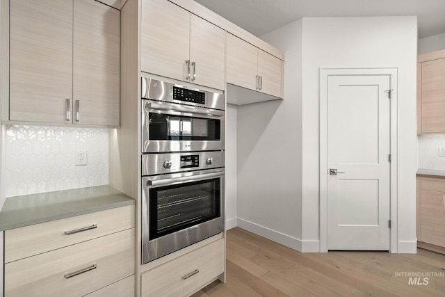 kitchen featuring light wood-style floors, decorative backsplash, stainless steel double oven, and light brown cabinetry