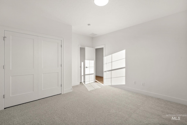 unfurnished bedroom featuring carpet floors, visible vents, baseboards, and a closet