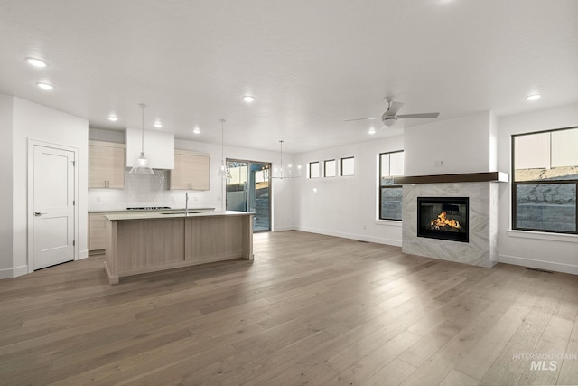 kitchen featuring decorative backsplash, open floor plan, a kitchen island with sink, light wood-type flooring, and a fireplace