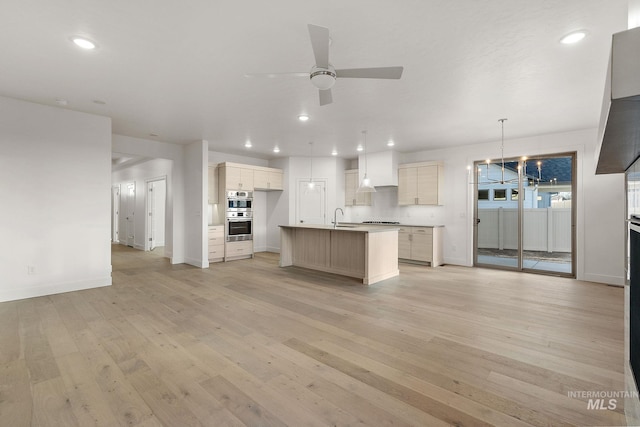 kitchen featuring a sink, a ceiling fan, open floor plan, light wood-type flooring, and an island with sink