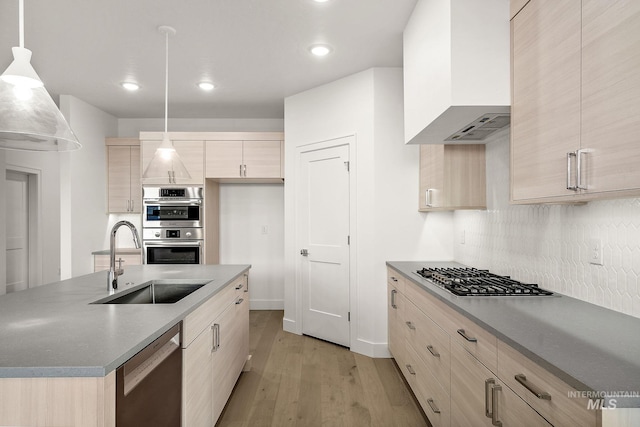 kitchen with light wood finished floors, custom exhaust hood, stainless steel appliances, light brown cabinets, and a sink