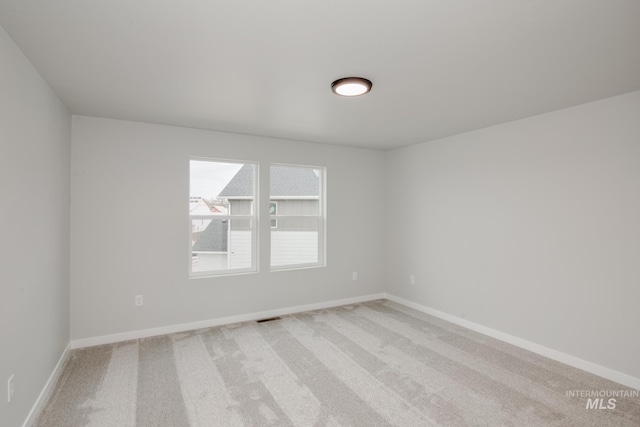 spare room featuring light colored carpet, visible vents, and baseboards