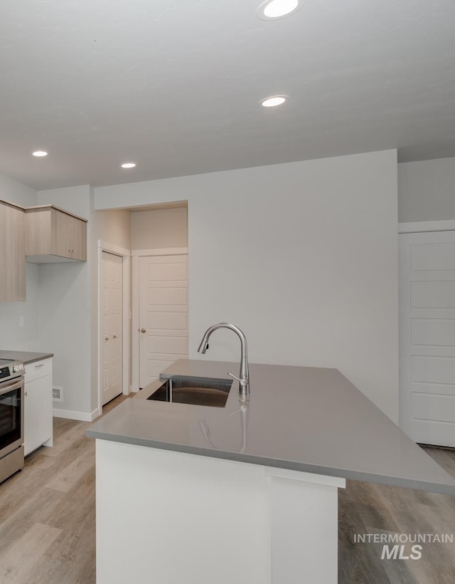 kitchen with light wood finished floors, modern cabinets, light brown cabinets, a sink, and recessed lighting