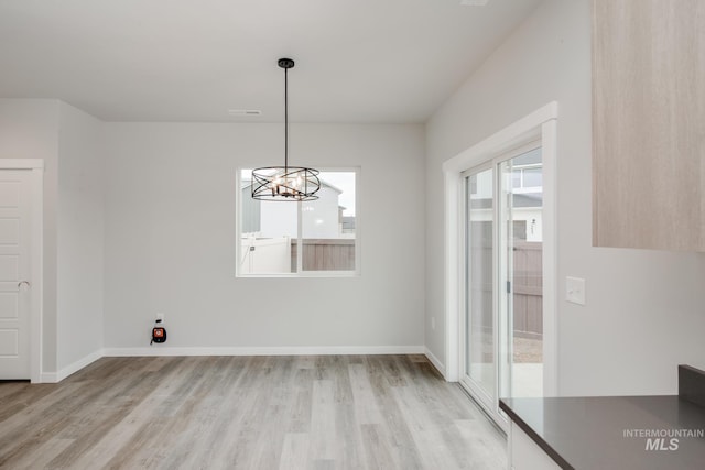 unfurnished dining area with a notable chandelier, light wood-type flooring, and baseboards