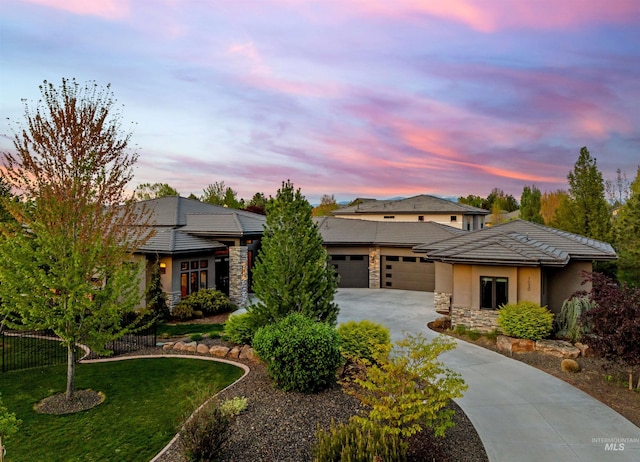prairie-style home with driveway, a garage, fence, stone siding, and stucco siding