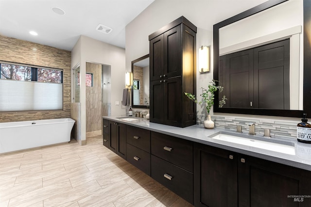 full bathroom featuring double vanity, visible vents, a freestanding tub, walk in shower, and a sink