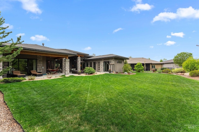 rear view of house with a patio, a yard, and stone siding