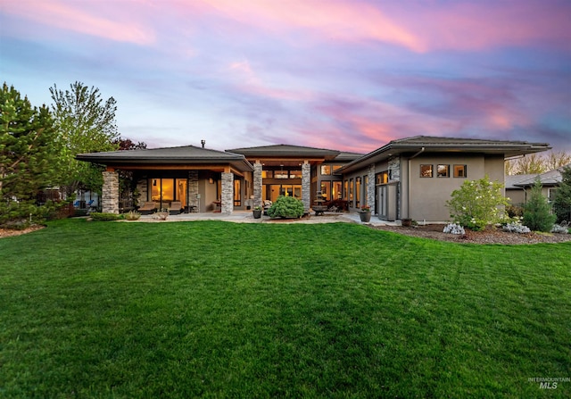 back of house at dusk featuring a lawn, stucco siding, and a patio
