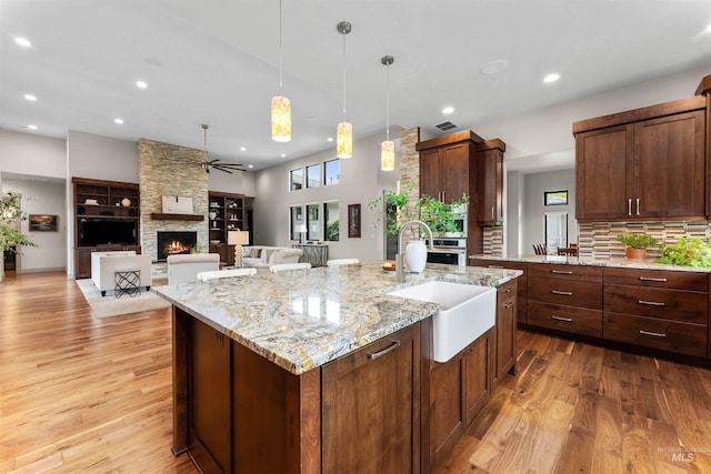 kitchen with ceiling fan, a sink, light wood finished floors, a fireplace, and a center island with sink