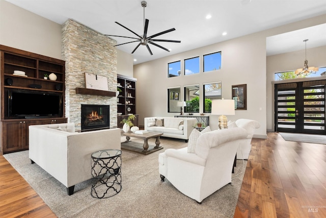 living area featuring a ceiling fan, a fireplace, wood finished floors, a high ceiling, and recessed lighting