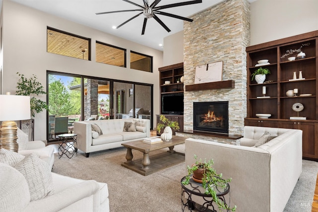 living area with carpet flooring, a ceiling fan, a stone fireplace, and a towering ceiling