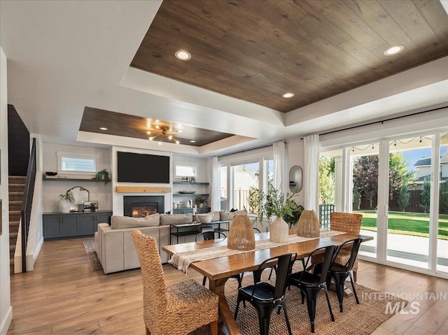 dining space with recessed lighting, a raised ceiling, wooden ceiling, a glass covered fireplace, and light wood-style flooring