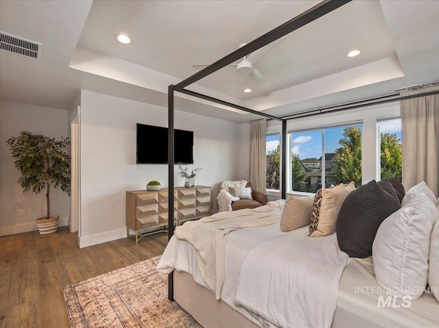 bedroom with a tray ceiling, visible vents, baseboards, recessed lighting, and wood finished floors
