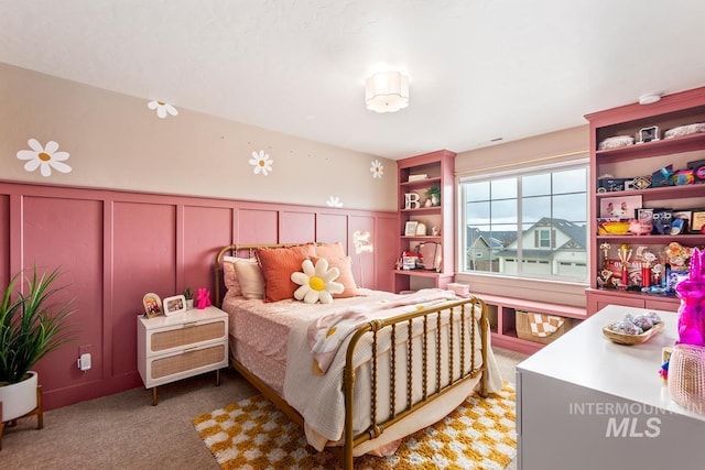 bedroom with wainscoting, light carpet, and a decorative wall