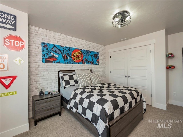 bedroom with visible vents, baseboards, light colored carpet, brick wall, and a closet