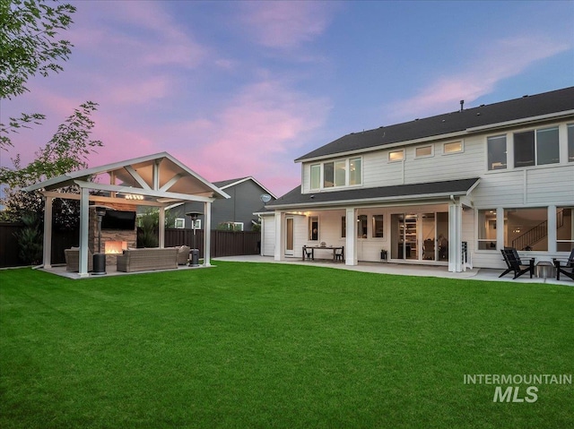 back of house at dusk with a lawn, fence, an outdoor living space, and a patio