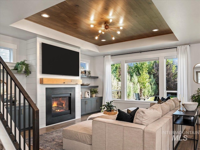 living area featuring stairway, wood finished floors, a glass covered fireplace, a raised ceiling, and wooden ceiling