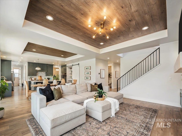 living area featuring a barn door, a raised ceiling, light wood-style flooring, and stairs