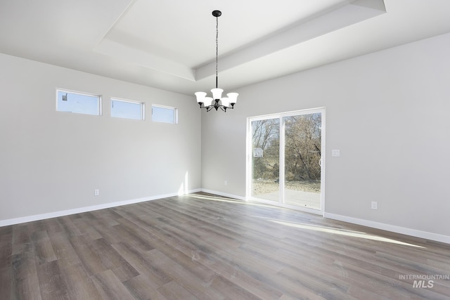 unfurnished room with a healthy amount of sunlight, hardwood / wood-style flooring, a tray ceiling, and an inviting chandelier