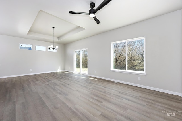 unfurnished room featuring ceiling fan with notable chandelier, a raised ceiling, and light hardwood / wood-style floors