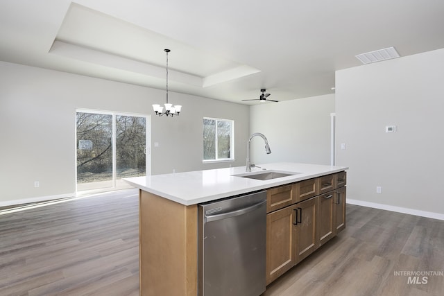 kitchen featuring stainless steel dishwasher, hanging light fixtures, a raised ceiling, sink, and a kitchen island with sink