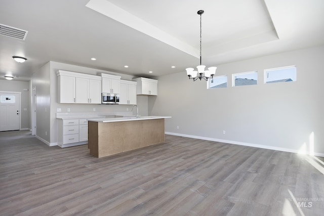 kitchen with a kitchen island with sink, white cabinets, decorative light fixtures, light hardwood / wood-style flooring, and a tray ceiling