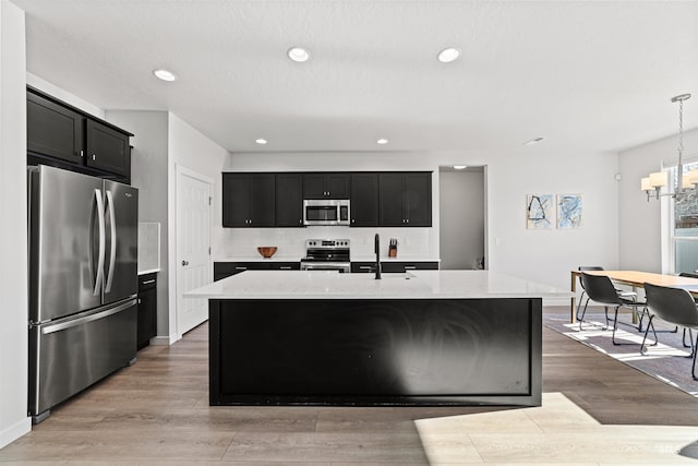 kitchen with a kitchen island with sink, sink, decorative light fixtures, and stainless steel appliances